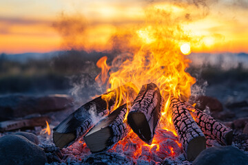 Fototapete - A fire is burning in a pile of wood, with the sun setting in the background