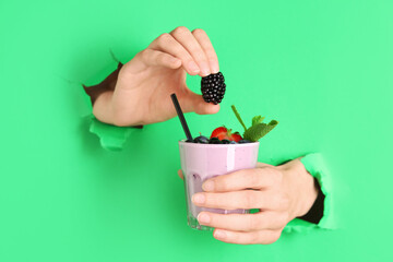 Wall Mural - Female hands holding glass of fresh smoothie with berries visible through torn green paper