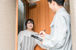© buritora - 訪問営業・セールスに来た作業着姿の男性を玄関で話を聞く笑顔の主婦
