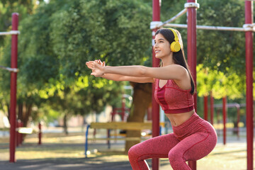 Wall Mural - Young woman in headphones training on sport ground