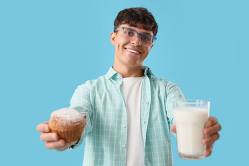 Wall Mural - Young man with glass of milk and tasty muffin on blue background