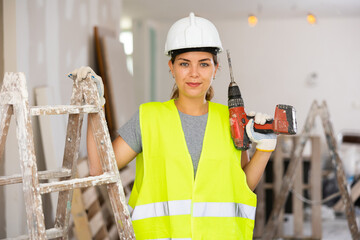 Female foreman in protective yellow vest and hard hat with a screwdriver in hand