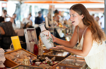 Wall Mural - Smiling female tourist looking at various vintage items at street flea market