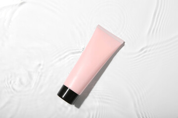 Sticker - Cosmetic product. Tube with cream in water on light background, top view