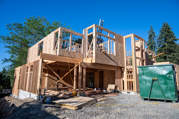 Wall Mural - Summer construction season, two story new house build in progress at the framing stage, messy job site with building materials and large dumpster out front
