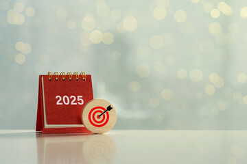 Happy New Year 2025 and goals. Target icon on a round wood block and white 2025 number on red small desk calendar.Business plans and goals and strategies that will lead to business success.