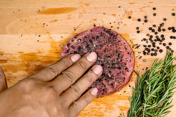 A hand is seasoning a tenderloin meat with pepper and salt