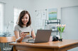 © Satori Studio - A young woman using a credit card to shop online with a laptop in a modern home office, surrounded by decor and natural light.