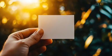 Hand holding blank white card with green foliage background.