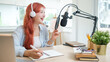 © wattana - Cheerful young woman in a headphone speaking into professional microphone mounted, recording a podcast  in her studio.