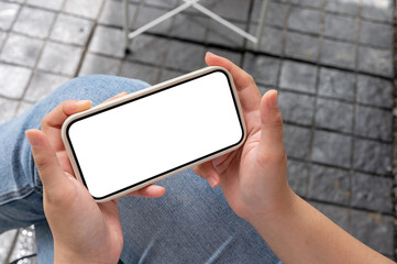 Wall Mural - A top view image of a woman in jeans sitting outdoors, watching a video on her smartphone.