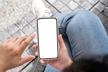 Wall Mural - Top view image of a woman in jeans sitting outdoors, using her smartphone, touching on the screen.