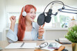 © wattana - Cheerful young woman in a headphone speaking into professional microphone mounted, recording a podcast  in her studio.