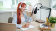 © wattana - Pretty young woman in a headphone speaking into professional microphone mounted, recording a podcast  in her studio.