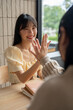 © bongkarn - A beautiful Asian woman is giving a high five to her friend while sitting together in a room.