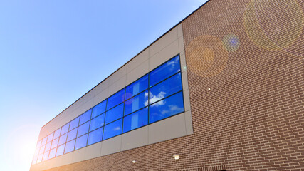 Wall Mural - Fragment of a modern building made of steel and glass. Abstract modern commercial architecture fragment. Walls made of shiny glass and steel under blue sky.