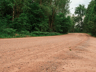 Wall Mural - A dirt road with trees in the background. The road is empty and there is no one on it. Country side way without proper asphalt surface.