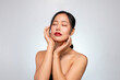 © bongkarn - A young Asian woman with a perfect, beautiful face, touching her face with her eyes closed.