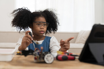 Wall Mural - Girl student learning and building project toy robotics technology at home. African American child girl training and control toy robot in classroom