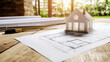 © AS Studio - A plastic model house sitting on a wooden table surrounded by blueprints and drafting tools, symbolizing the planning of a new home