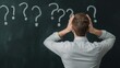 © Pojjanee - Overwhelmed by Questions: A man stands before a blackboard filled with question marks, his hands on his head, depicting the feeling of being overwhelmed and unsure.