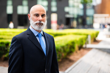 Mature bald stylish business man portrait with a white beard outdoor in a green city