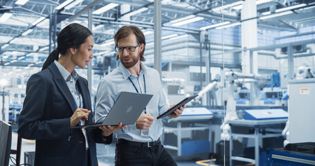 Fototapete - Male Engineer and Female Project Manager Standing in Office, Talking, Using Computers and Monitoring Production at Modern Automated Electronics Manufacture with AI Robotic Arms