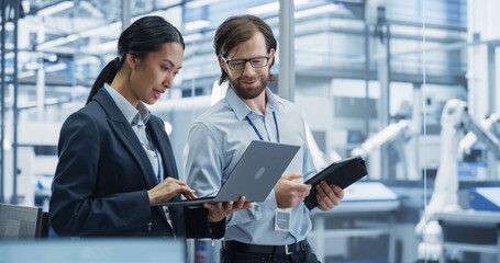 Fototapete - Industrial Engineers Working at Technology Factory. Caucasian Man and Asian Female Using Laptop and Tablet Computers and Having a Conversation. Footage with a Portrait of a Couple of Employees