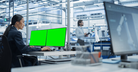 Fototapete - Female Robotics Technician Working on Desktop Computer with Green Screen Chromakey Mock Up Display in a Factory Office. Technological Research and Development Facility with Autonomous Assembly Line