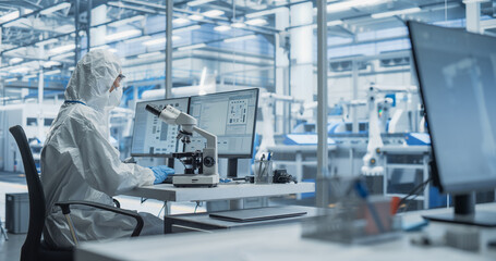 Fototapete - Modern Factory: Industrial Engineer Working on Desktop Computer in Clean Sterile Coveralls. Scientist Using a Microscope, Developing Advanced Solutions for High Tech Medical Vaccine and Gene Research