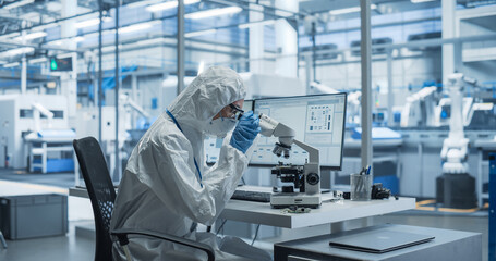 Fototapete - Research Factory Cleanroom: Engineer Wearing Coveralls, Gloves, and Goggles while Using Microscope to Inspect a Microchip. Scientist Developing an Advanced Electronics Component for Precision Industry