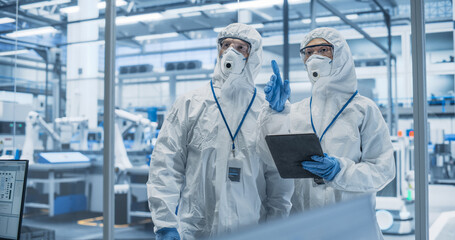 Fototapete - Industrial Scientists Wearing Disposable Protective Suits, Masks and Goggles at a Production Plant. Specialist Using Tablet Computer, Analyzing Potential Work Hazards and Contamination at a Workplace