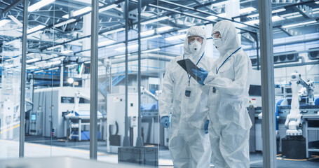 Fototapete - Development Factory Cleanroom: Engineers Wearing Coveralls and Goggles while Talking and Using Tablet. Scientists Working in Advanced Electronics Manufacture with Precision Machinery