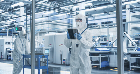 Fototapete - Portrait of a Female Worker Wearing Full-Body Protective Coveralls, Mask and Goggles at a Biotechnology Manufacturing Plant. Young Specialist Using a Tablet Computer, Overlooking Nanotech Production