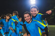 © PoppyPix - Teenage girls during training football. Team of laughing girls jumping on each others back, feeling joy and showing their fists and unity for victory. High quality photo