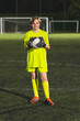 © PoppyPix - full vertical shot of a young goalkeeper girl in a yellow uniform holding a ball and posing, evening practice. High quality photo