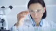 © volha_r - Scientist female researcher with protective glasses examining lab tube with a blue fluid. Microbiology and science concept