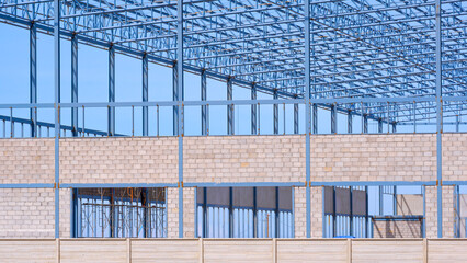 Wall Mural - Metal columns and roof beam with block wall structure of incomplete industrial factory building and precast concrete fence in construction site against blue sky background, perspective side view