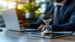 © Earny - A businessman works on a laptop with an hourglass, symbolizing time management and productivity in a modern office environment.