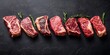 © phurinee - Top view of a variety of raw Black Angus Prime meat steaks, including T-bone, tomahawk, and New York steak, showcasing marbled beef strip loin steaks.