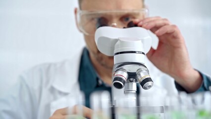 Man scientist with protective glasses using microscope in laboratory. Microbiology science concept