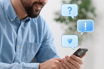 Canvas Print - Happy man sending message via smartphone at home, closeup. Speech bubbles near device