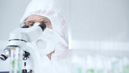 Professional scientist in protective gear is using microscope in a laboratory setting, close-up of researcher. Science and medicine concepts