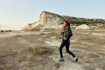 Wall Mural - Woman in hat and jeans walking in desert with mountain in background