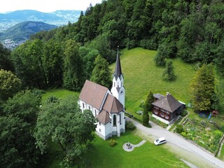 Wall Mural - Aerial view of Kuratienkirche Meschach surrounded by lush greenery. Gotzis, Austria