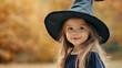 © Ratchpon - A young girl wearing witch hat smiles joyfully in warm autumn setting. Her expression is playful and enchanting.