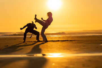 Two people practicing capoeira martial arts on the beach at sunset