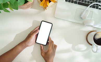 Wall Mural - Overhead view of hands holding smartphone with blank screen on white office desk.