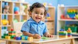 © Man888 - A smiling Hispanic baby boy in a bright blue shirt and khaki pants sits at a tiny desk, surrounded by colorful toys and learning blocks.