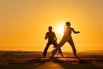 Couple practicing capoeira martial art at sunset on the beach